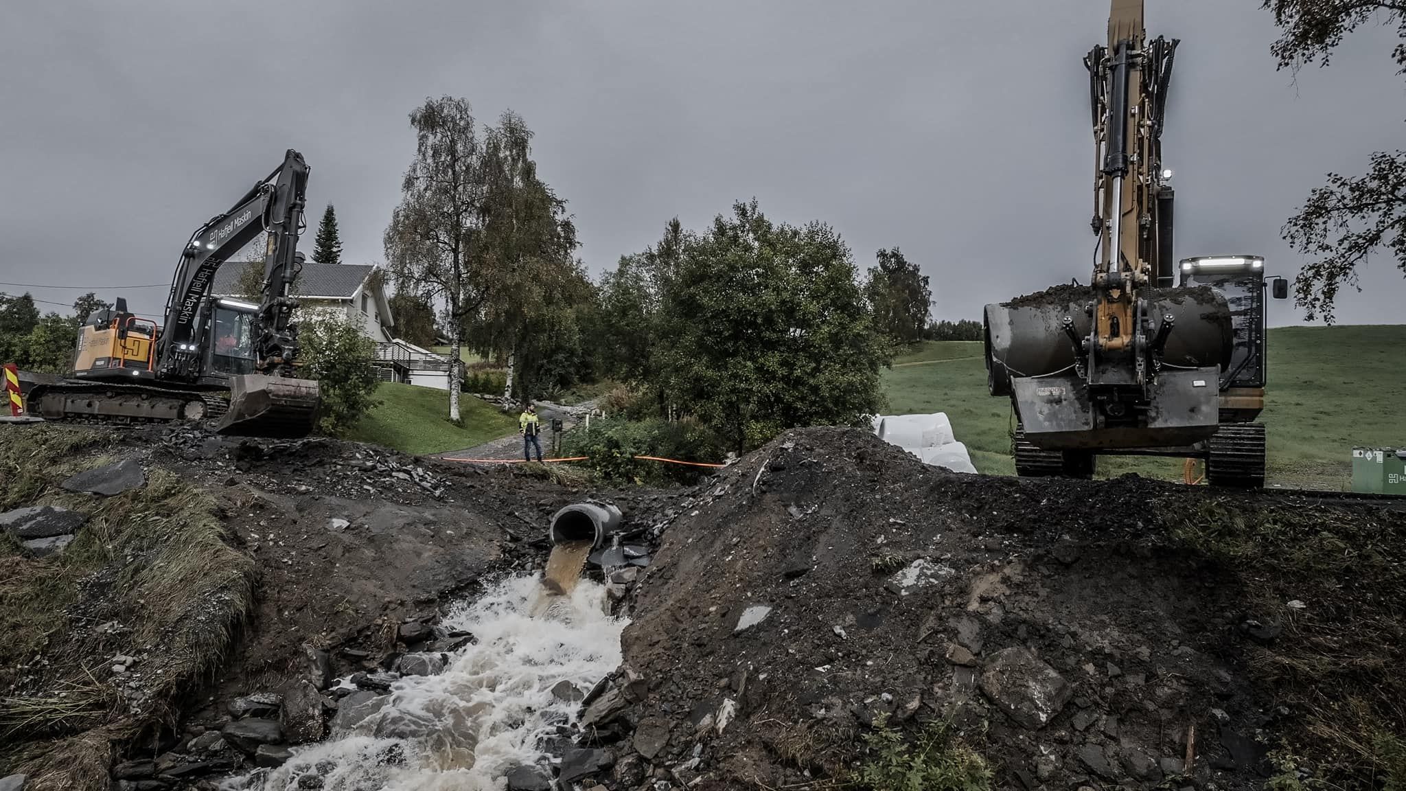 To gravemaskiner sikrer grunnen etter flom med rennende vann